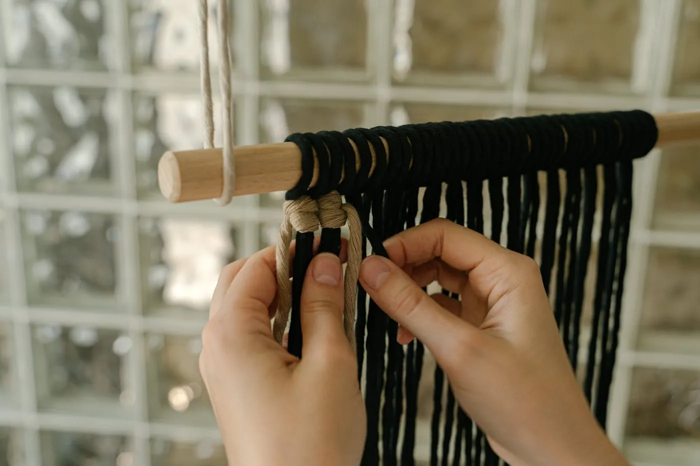 Manos tejiendo macramé sobre telar vertical