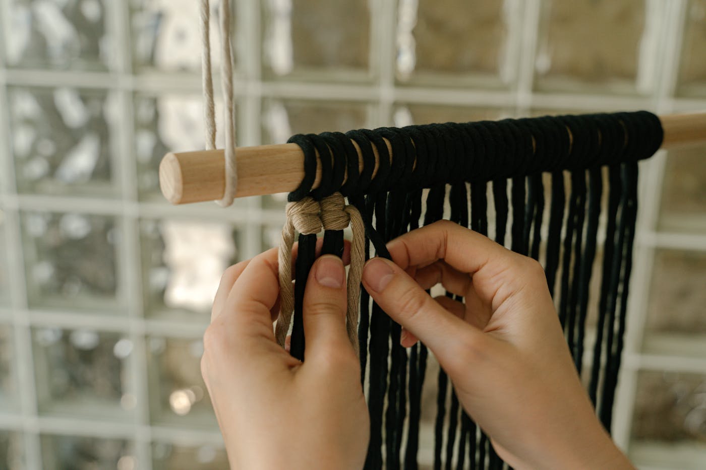 Manos tejiendo macramé sobre telar vertical